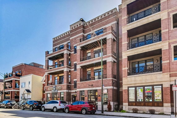 Front view of a multi-story brick building with balconies and ground-level shops.