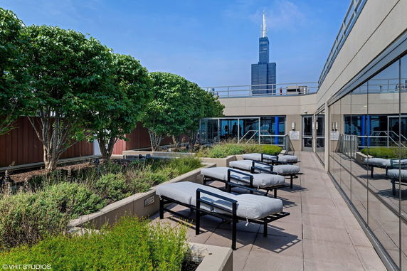 Rooftop area with lounge chairs, greenery, and cityscape view in the background.