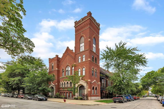 Front view of a red brick multi-story building with arched windows and a tower.