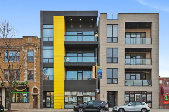 Front view of a modern multi-story building with yellow accents and balconies.