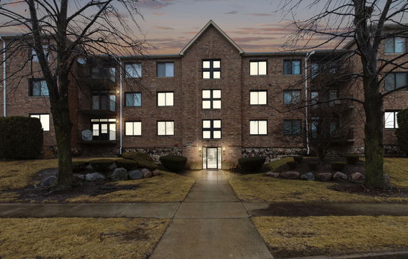 Front view of a multi-story brick building with lit windows.