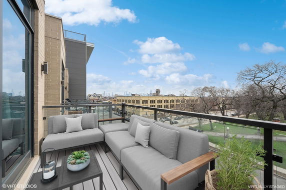 Panoramic view from a balcony with outdoor seating, overlooking cityscape and park.