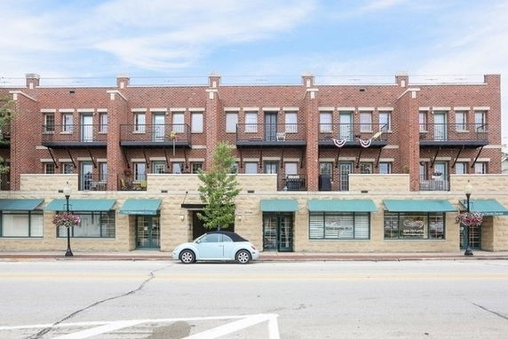 Front view of a multi-story brick building with balconies and ground-level shops.