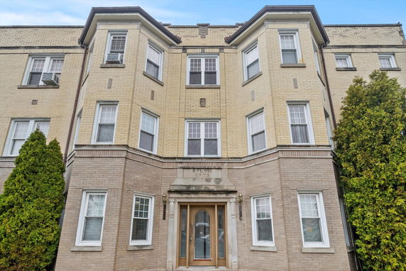 Front view of a multi-story brick apartment building with multiple windows and a central entrance.