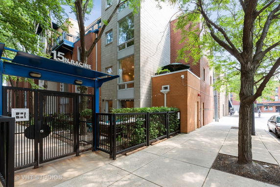 Front view of a multi-story residential building with an entrance gate and surrounding trees.