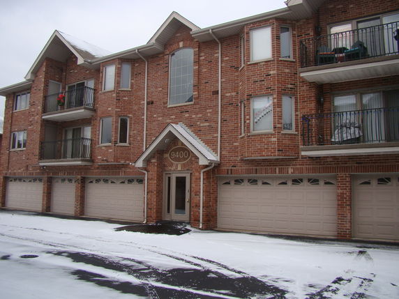 Front view of a three-story brick building with multiple balconies and garages.