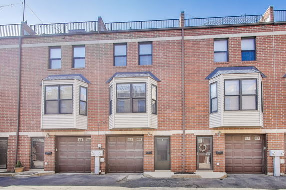 Front view of a brick townhouse with multiple garage doors and bay windows.