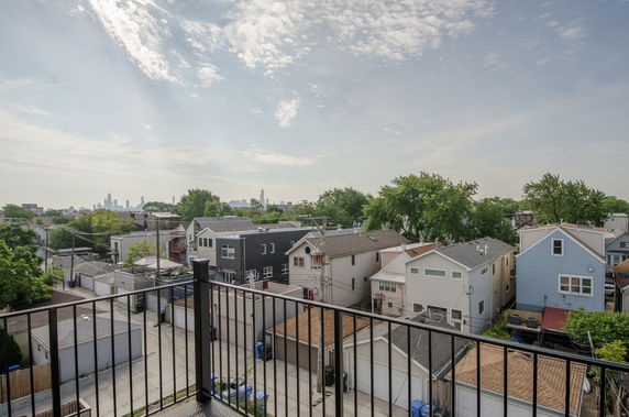 Panoramic view from a balcony overlooking a neighborhood with houses and distant city skyline.