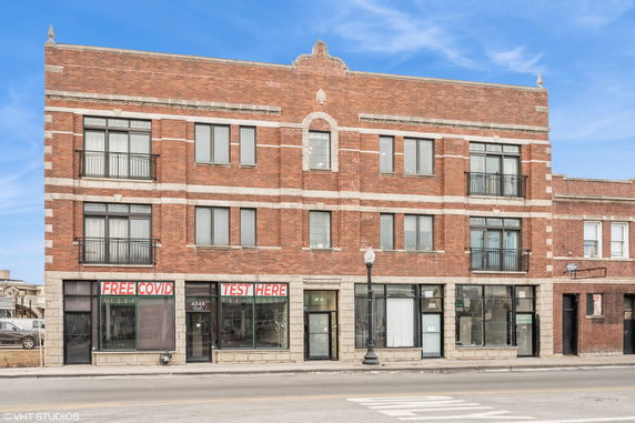 Front view of a multi-story brick building with large windows and ground floor commercial spaces.