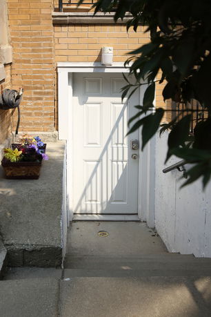 Exterior view of a white door set in a brick wall at a basement level.