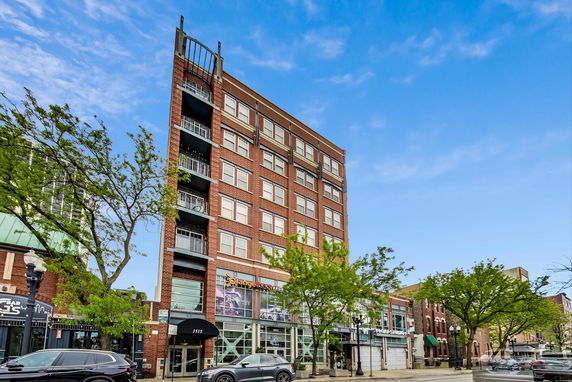 Front view of a multi-story brick building with balconies and commercial spaces on the ground floor.
