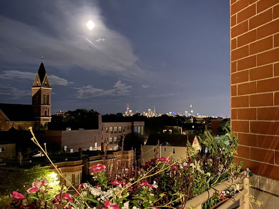 Nighttime panoramic view of city skyline with prominent church tower in the foreground.