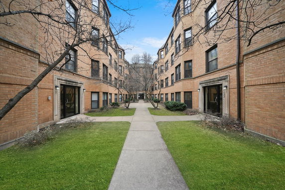 Front view of a multi-story brick apartment building with a central walkway and grass.