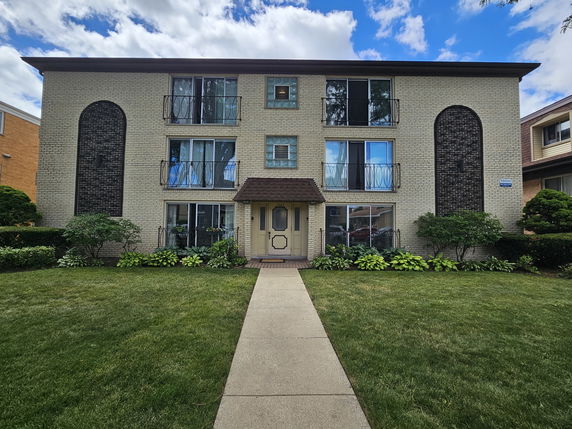 Front view of a three-story residential building with balcony railings and a central entrance.
