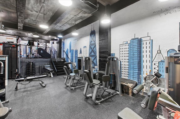 Indoor gym with various exercise equipment and a mural of city buildings on the wall.