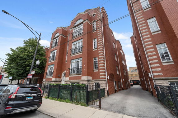 Front view of a multi-story brick apartment building with decorative railings and arched windows.