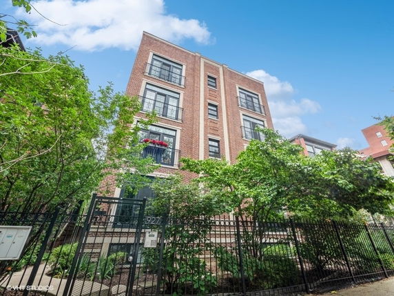 Front view of a multi-story brick building with large windows and a gated entrance.