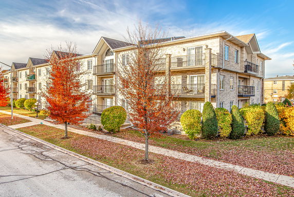 Front view of an apartment building with balconies and autumn foliage.
