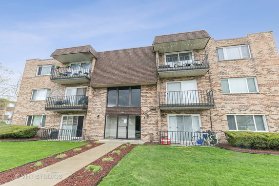 Front view of a three-story brick apartment building with balconies.