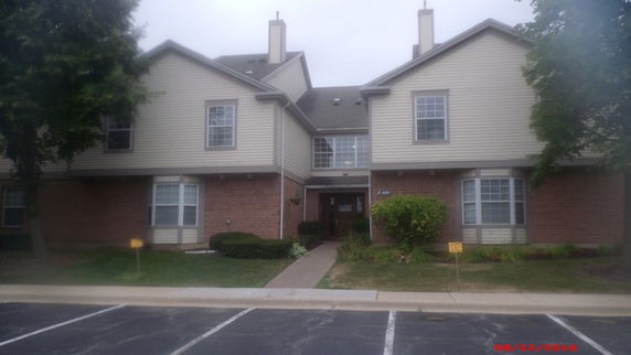 Front view of a two-story residential building with multiple entrances and parking space in front.