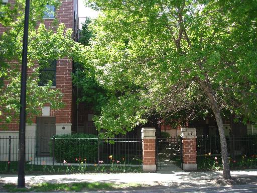 Front view of a brick building partially obscured by trees and a fence.