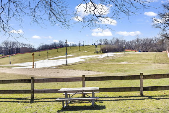 Outdoor view of an open field with patches of snow on a sloped area near a wooden fence and a picnic table.