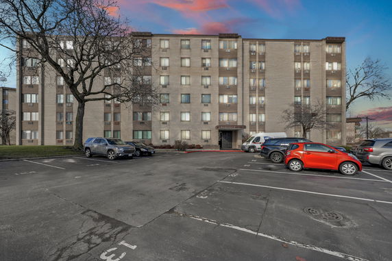 Front view of a multi-story apartment building with parked cars in front.