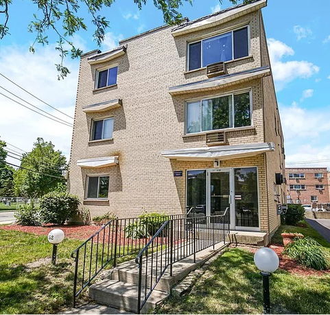 Front view of a three-story apartment building with multiple windows and a small entrance ramp.