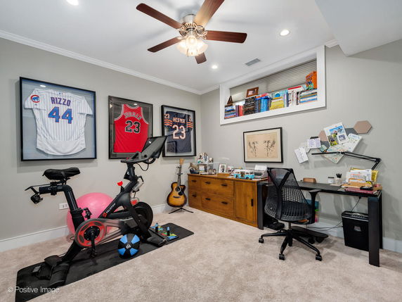 Indoor room with exercise bike, framed jerseys, office desk, and chair.