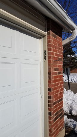 Partial view of a brick house with a garage door and visible number 89 on the wall.