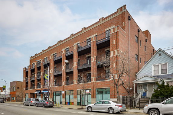 Front view of a multi-story brick building with balconies and street-level shops.
