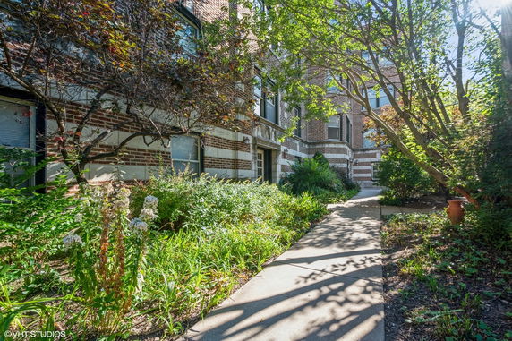 Front view of a brick building with greenery and a walkway.
