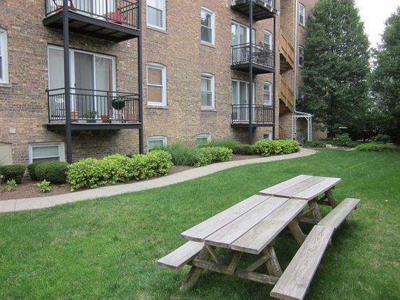 View of a multi-story brick building with balconies and a picnic table in the foreground.