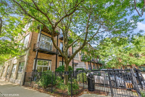 Front view of a three-story brick building with balconies and a black metal fence.