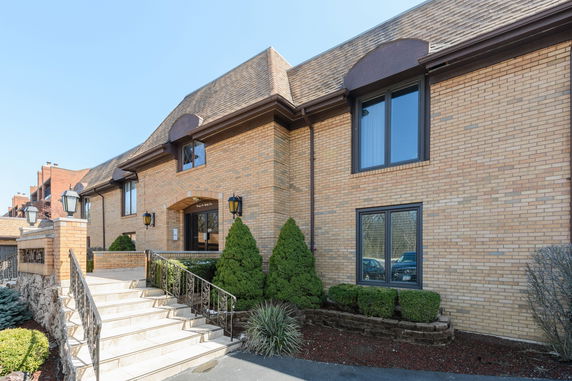 Front view of a multi-story brick building with a sloped roof and a staircase leading to the entrance.