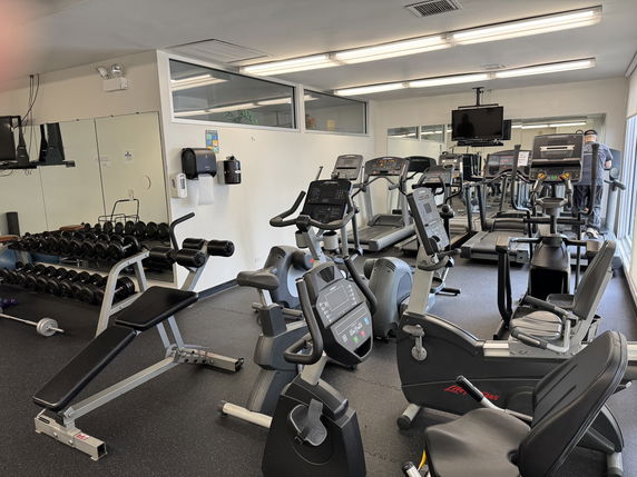 Interior view of a gym with exercise equipment including treadmills, stationary bikes, and weights.