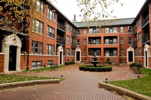 Front view of a multi-story brick apartment building with arched doorways and a courtyard.