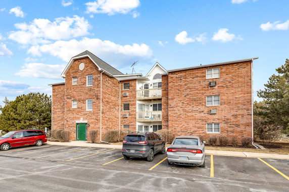 Front view of a multi-story brick apartment building with parking area.