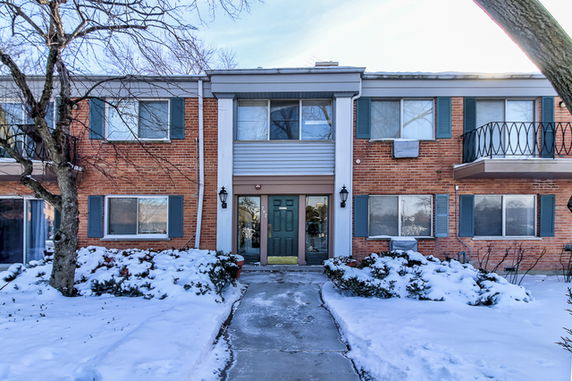 Front view of a two-story brick house with a central entrance and green shutters, surrounded by snow.