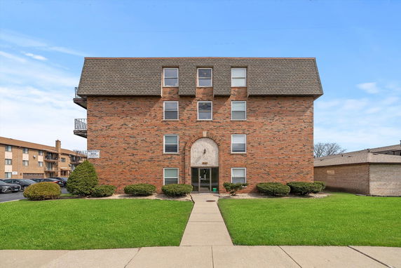 Front view of a multi-story brick apartment building with a sloped roof.