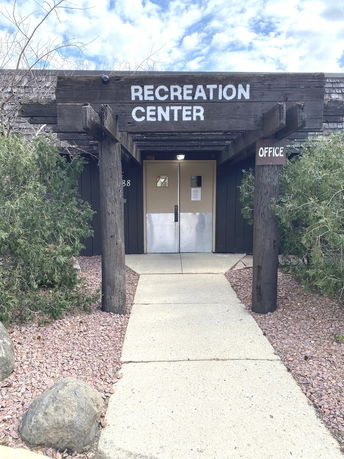 Front view of a recreation center entrance with wooden beams and shrubbery.