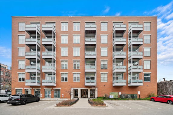 Front view of a multi-story residential building with balconies and parking area.
