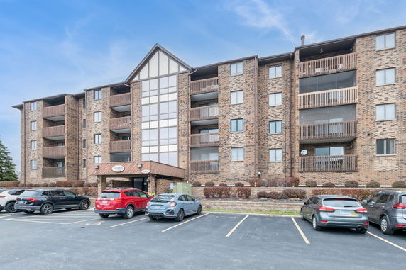 Front view of a multi-story brick building with balconies and a parking area.