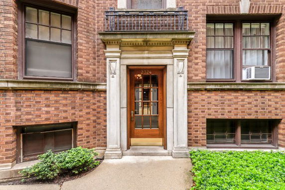Front view of a brick building entrance with a wooden door and decorative columns.