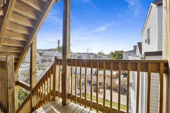 Wooden balcony on a house overlooking nearby rooftops and a backyard area.