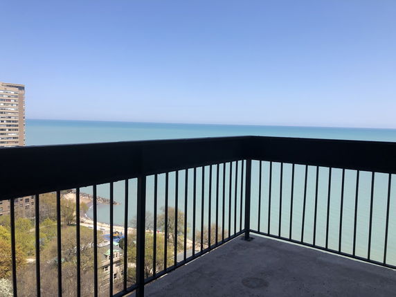 Wide angle view of a balcony overlooking a large body of water with clear skies.