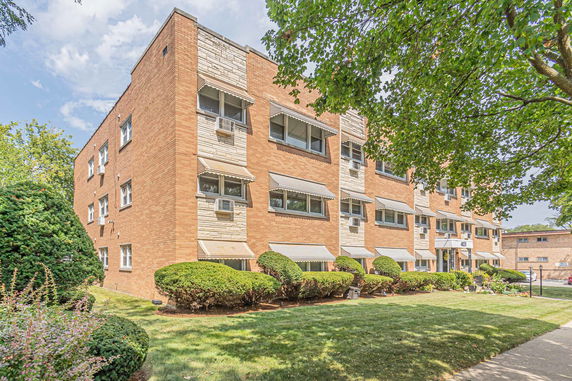 Front view of a multi-story brick apartment building with multiple windows and air conditioning units.