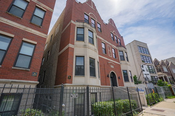 Front view of a multi-story brick building with arched windows and a gated entrance.