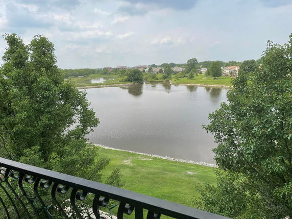 Panoramic view of a lake surrounded by trees and houses as seen from a balcony.