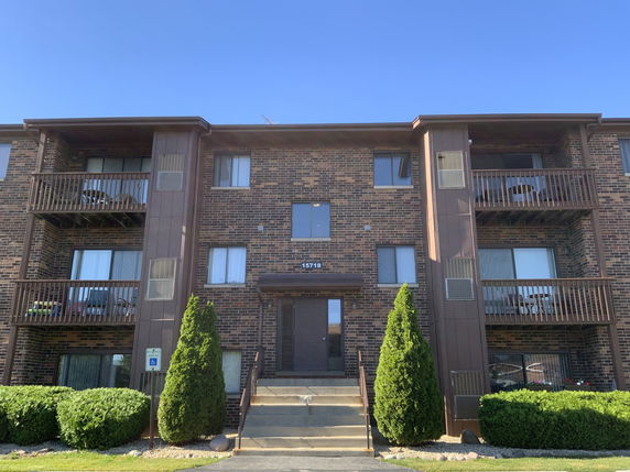 Front view of a three-story brick apartment building with balconies.